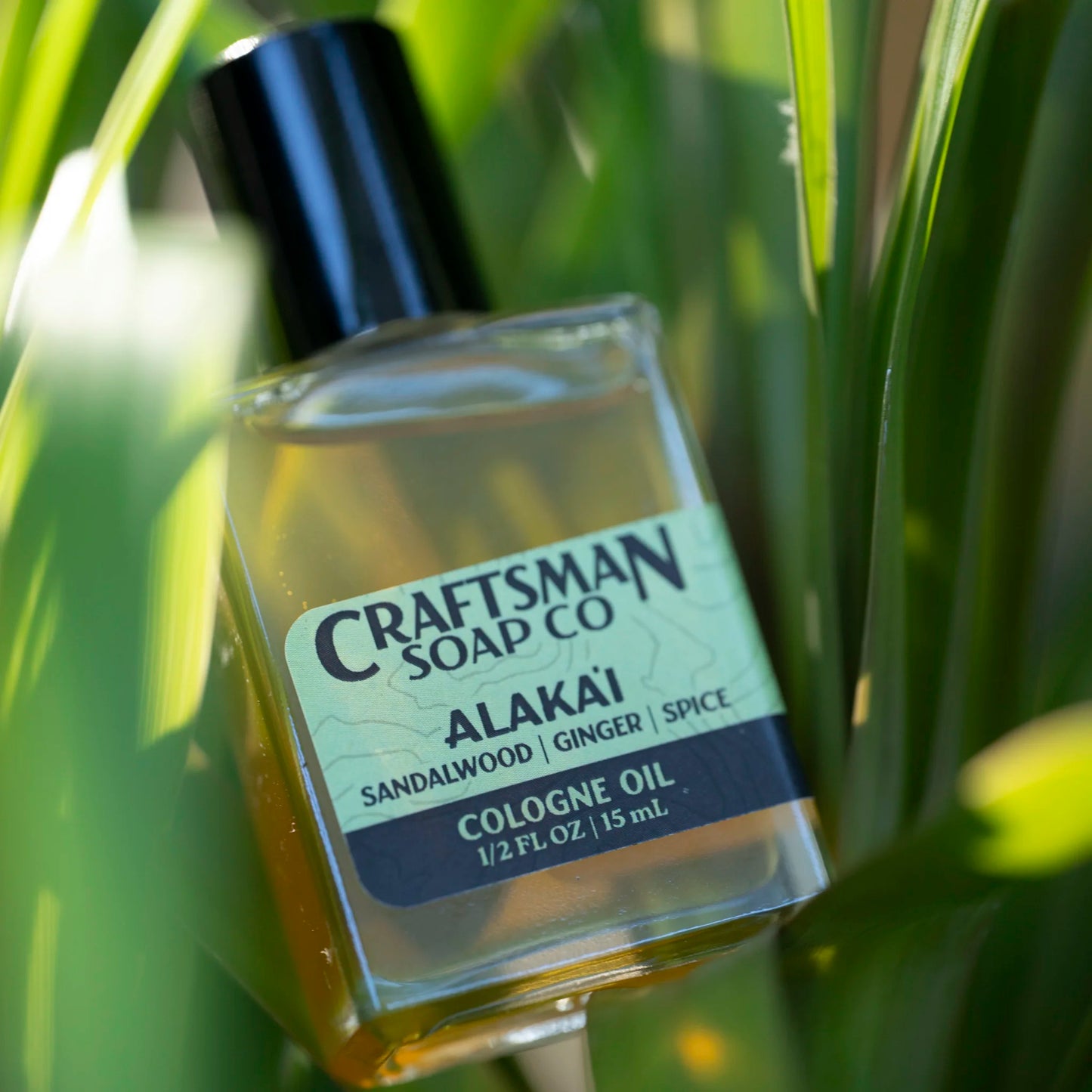 Craftsman Soap Co. Alakaʻi Cologne Oil clear glass roller ball bottle among tropical grass — Hawaiian wilderness essential oil cologne with sandalwood and vetiver
